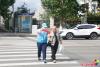 9月18日，在延吉市局子街北大市場西側的十字路口旁，大學志愿者劉書達頭戴志愿者標志帽、身穿藍馬甲、佩戴綬帶和袖標，手拿小紅旗，在路口維護交通秩序，引導行人通過斑馬線安全過馬路。
